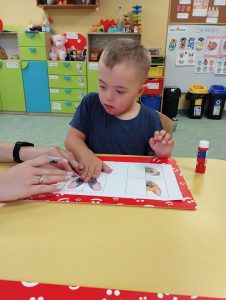 Chłopczyk robi pracę plastyczną z małą pomocą