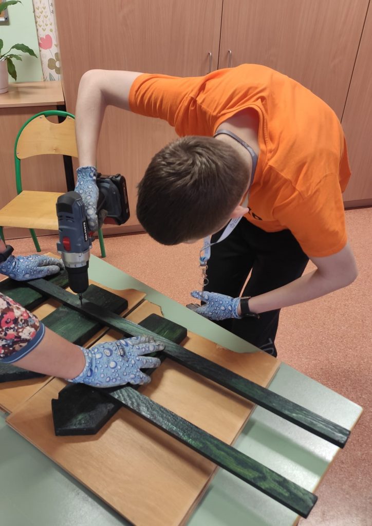 uczniowie skręcają drewniane elementy na dekorację do szkolnego ogrodu