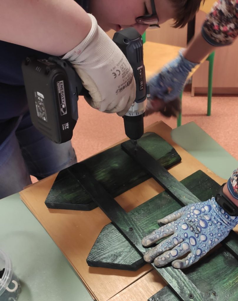 uczniowie skręcają drewniane elementy na dekorację do szkolnego ogrodu